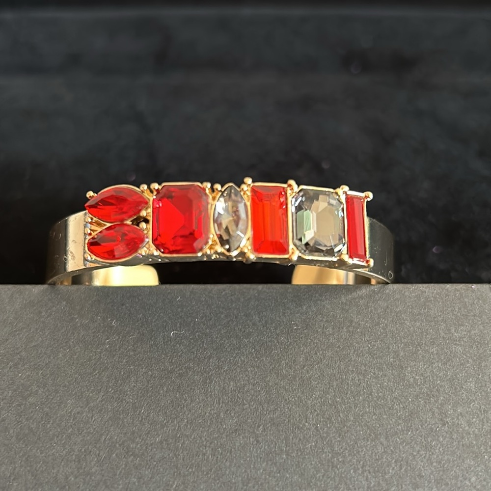 Gold jeweled slip on cuff bracelet with red and grey bezel set stones.
